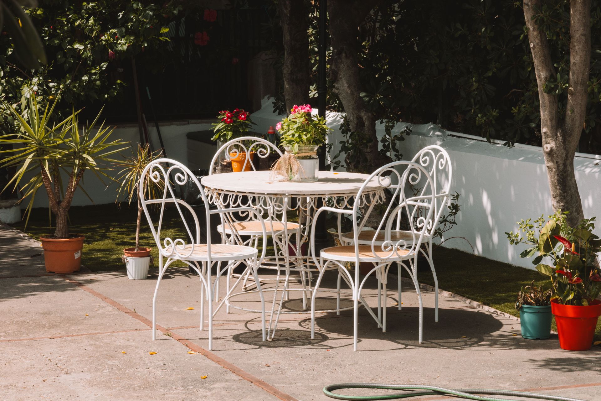 White wrought iron furniture surrounded by plants in a sunny café garden.