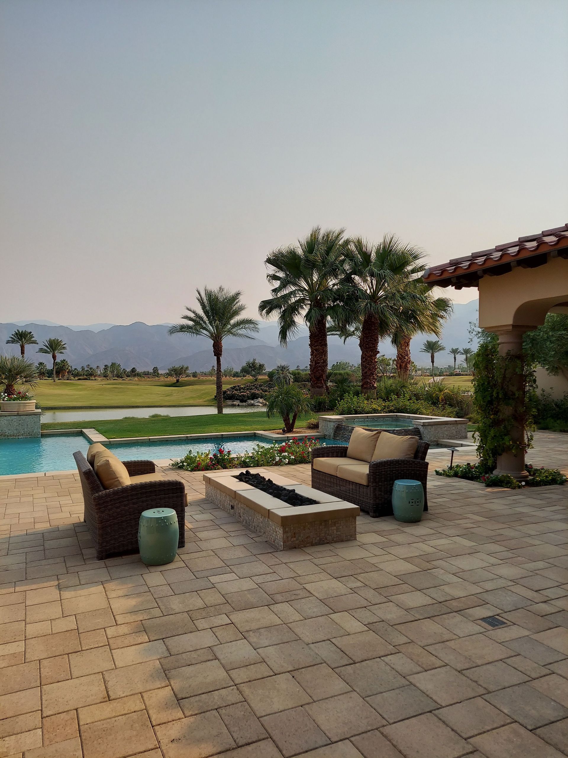 Serene outdoor patio with pool, wicker seating, and palm trees against mountain backdrop.